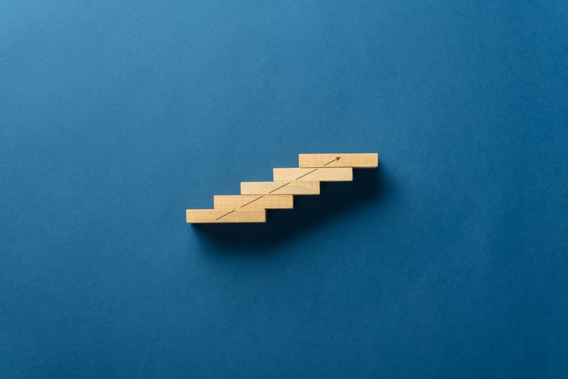 Business vision and success concept Wooden pegs placed in a stairway like structure with a rising arrow drawn on it. Over blue background with plenty of copy space.