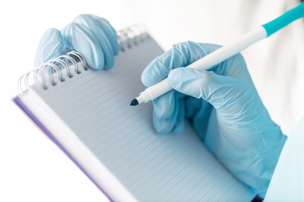 Female hand in a medical glove holds a tablet for writing and a pen. Medicine concept