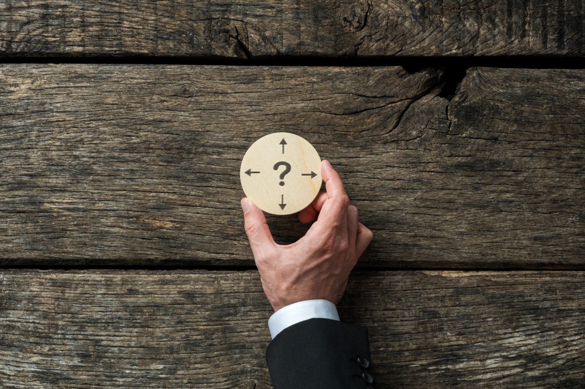 Business planning and decision conceptual image - businessman holding wooden cut circle with question mark and arrows pointing in different directions on it.