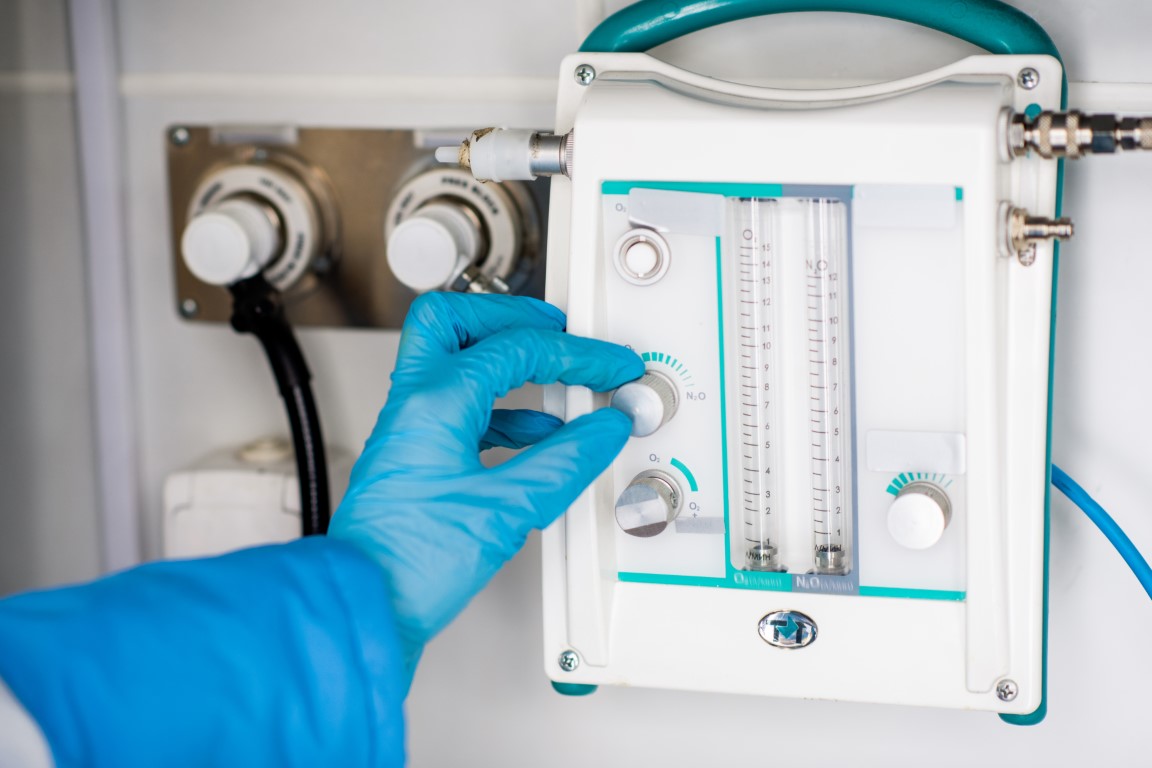 Gloved hand of paramedic regulating level of something on medical first aid equipment inside ambulance car